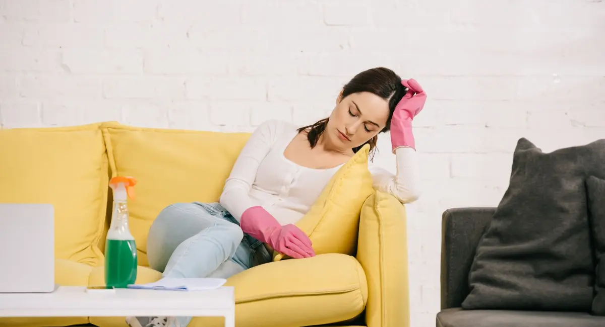 An image of a woman in cleaning gloves collapsed on a sofa