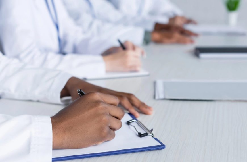 An in of a few doctors in a row zoomed in on them writing on clipboards: Call the Doctor