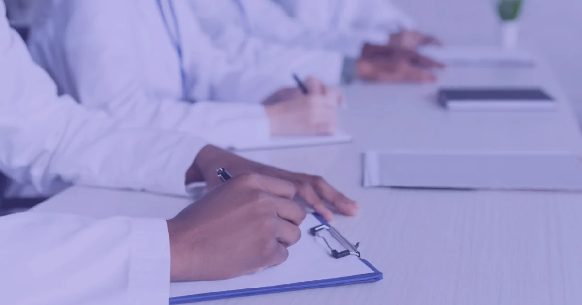 Doctors in white coats writing notes on clipboards at a conference table.