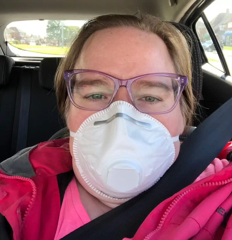 Susan with blonde hair in purple glasses, white mask and red jacket with seatbelt on, suburban view outside, capturing anxious pandemic dentist trip.