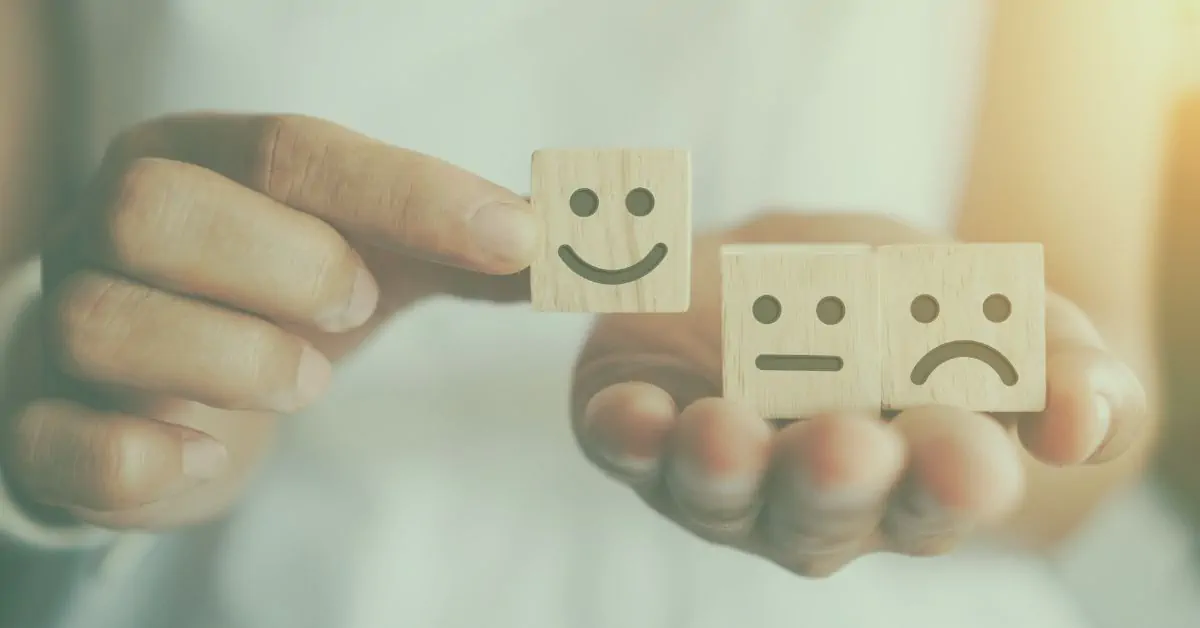 Hand selecting wooden smiley block over sad and neutral faces – illustrating emotional impact on fibromyalgia symptom control.