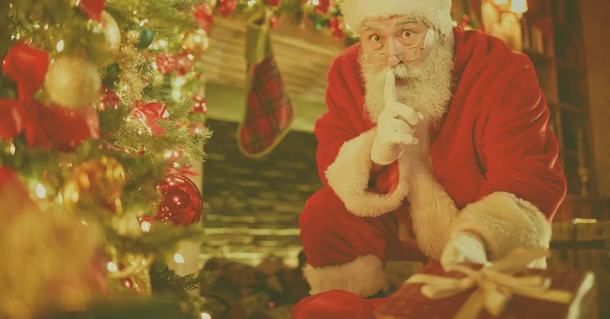 Father Christmas in red suit and hat peeking playfully beside watercolour snowy evergreen Christmas trees on sage green background